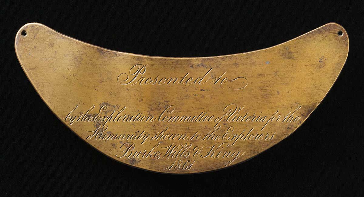 Golden crescent-shaped metallic plate inscribed with th words 'Presented to (blank) by the Exploration Committee Victoria for the Humanity shewn to the Explorers Burke, Wills & King 1861'.