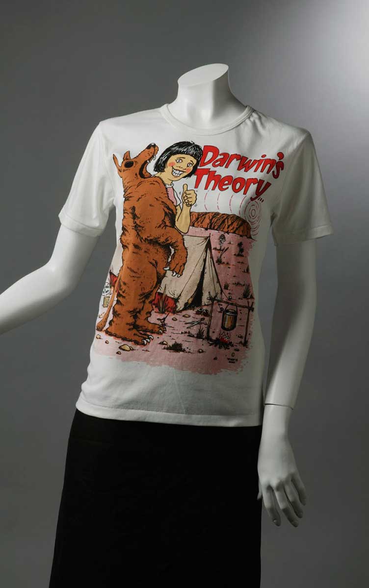Souvenir T-shirt which reads 'Darwin's Theory' and shows a woman resembling Lindy Chamberlain giving the thumbs up while holding a dingo skin, outside a tent. - click to view larger image