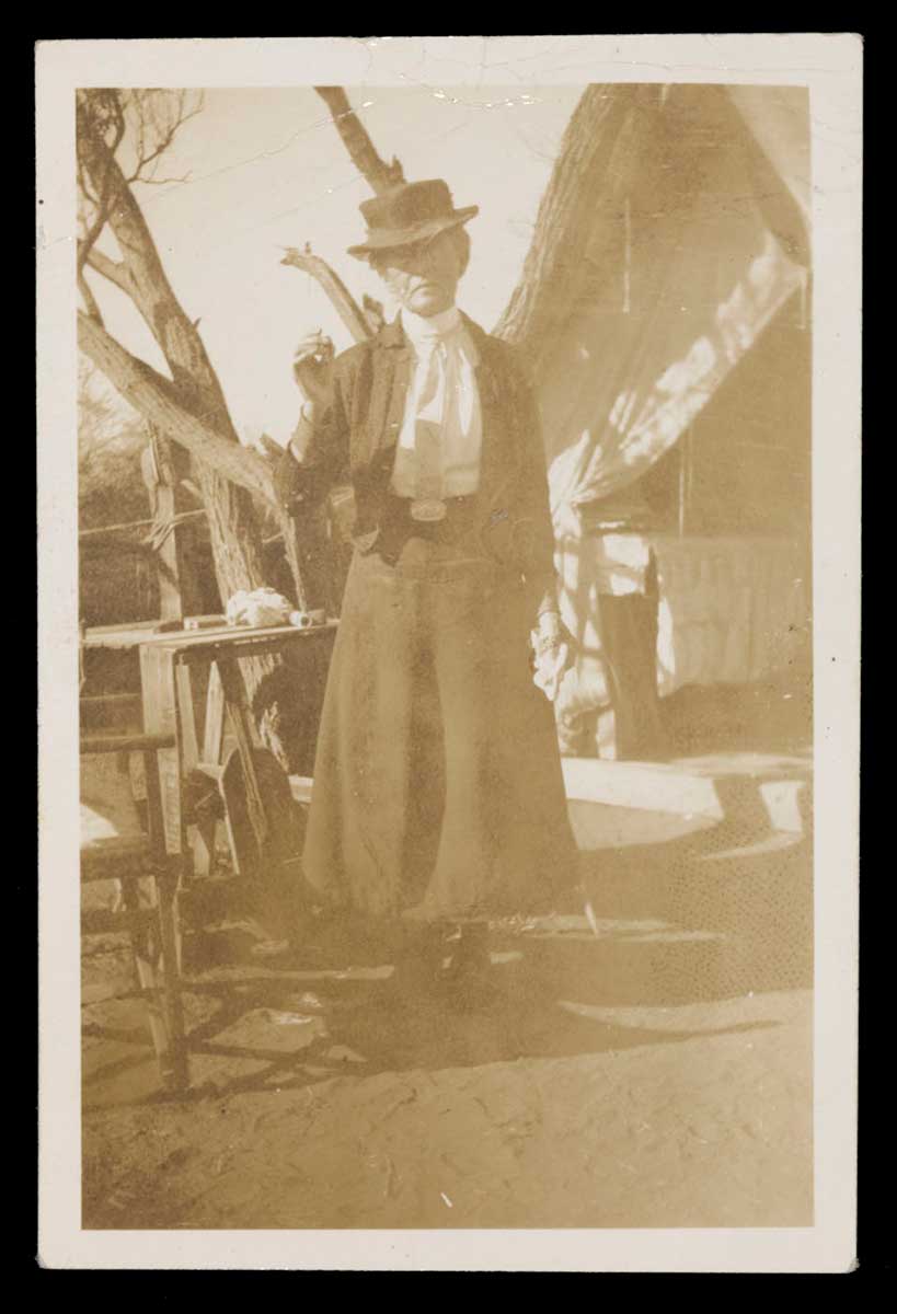 Sepia photograph showing a woman standing in front of a canvas tent. - click to view larger image