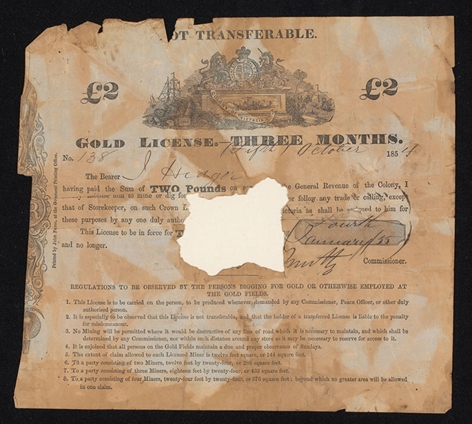 Photograph of a 'GOLD LICENSE' printed on paper, which has been folded and torn around the edges and has a section missing at the centre. A 'Colony of Victoria' coat of arms is centre top, wth printed and handwritten text underneath.