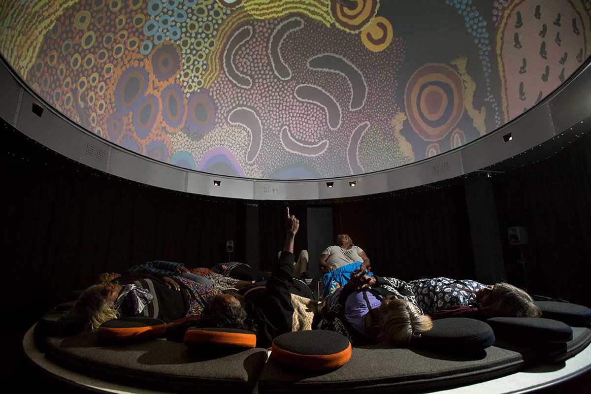 Group of women lying on padded surfaces and looking up at a dome with a digital screen - click to view larger image