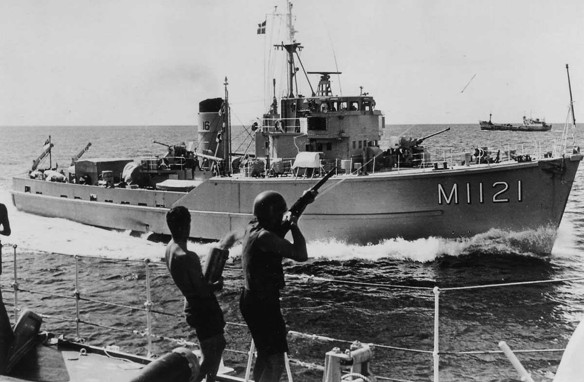 Photo taken from deck of ship at sea with two sailors in foreground. About 100 metres away is a RAN patrol boat.