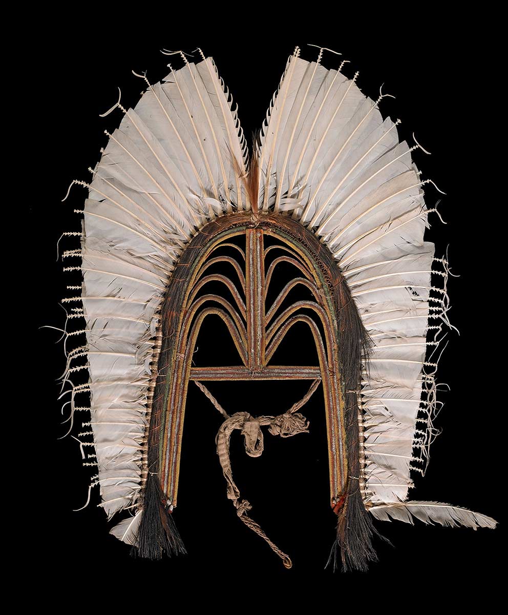 Headdress made of an open-work frame of bound cane with white feathers round the edge. Cassowary plumes are bound round the junction. The frame is painted red, yellow and white. - click to view larger image