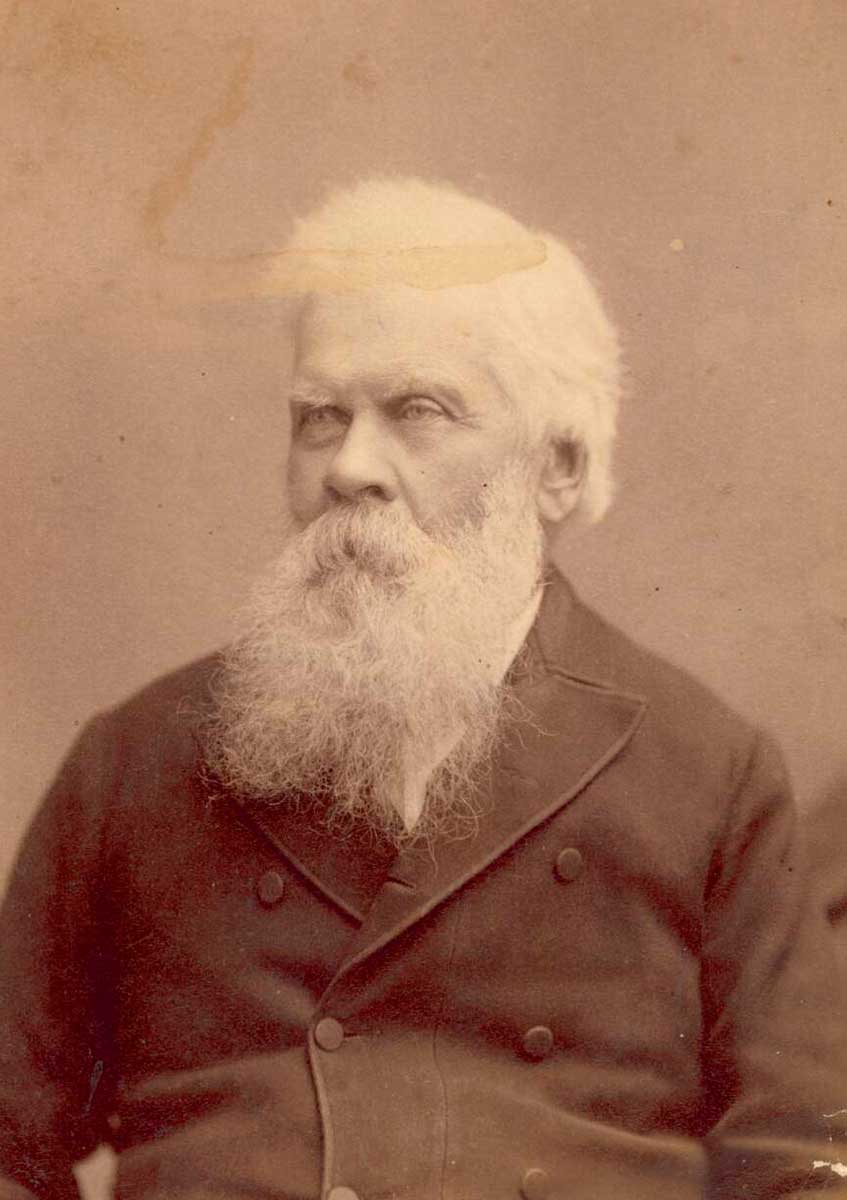 Black and white photo with sepia tone of a man with a long white beard and wearing 19th century clothing. - click to view larger image