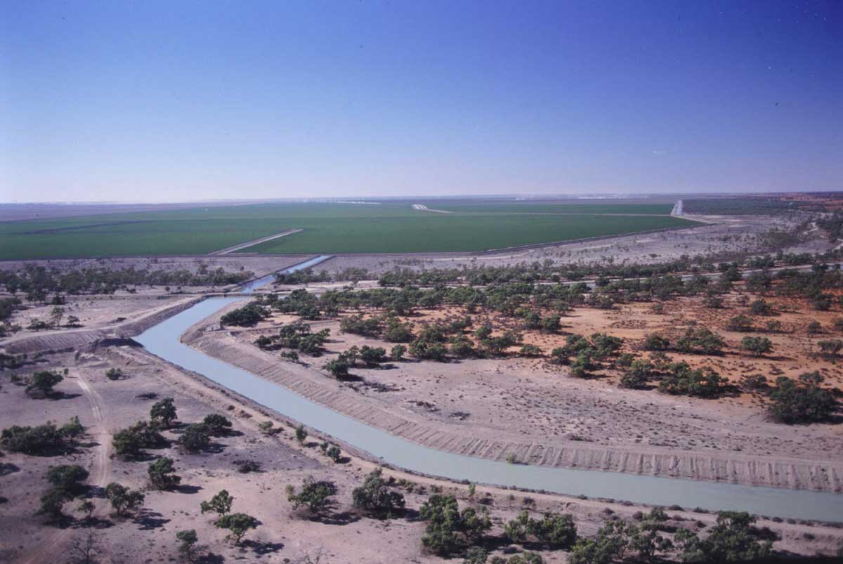 Colour photo of panorama view of farmland featuring an artificial canal running towards lush paddocks in the distance.