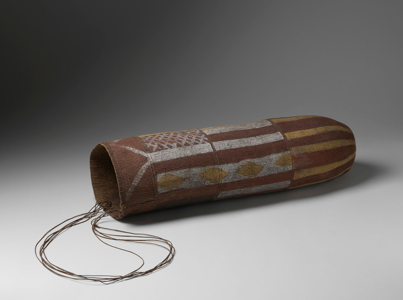 A cylindrical fibre basket with a string handle. The basket has been painted with ochre. - click to view larger image