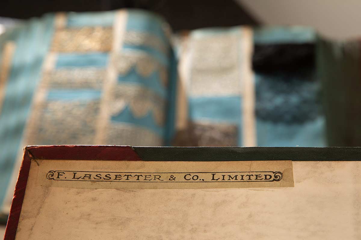 Colour photograph of a storage box with a label printed with the text: F. LASSETTER & CO., LIMITED. There is a blurred image in the background of textile samples. - click to view larger image