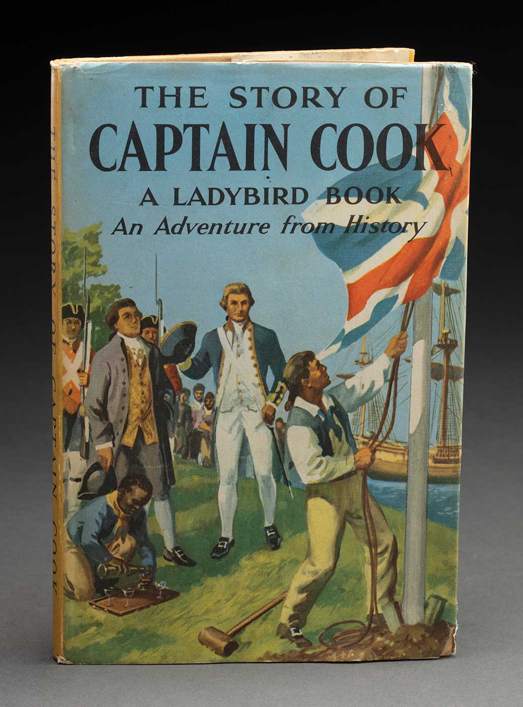 A book with a colourful cover featuring a man raising a Union Jack flag and with captian cook depicted beside him. Text of the cover reads 'THE STORY OF CAPTAIN COOK / A LADY BIRD BOOK / ...' - click to view larger image