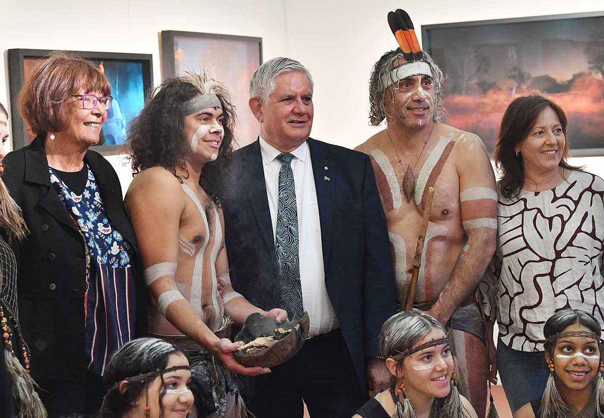 Member of Parliament Ken Wyatt poses with a group of people, some who are wearing face and body paint and traditional attire.