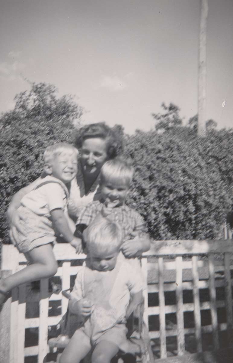 Small black and white photo of a woman and three children by a fence. - click to view larger image