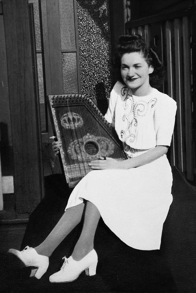 Black and white photograph of a smiling young woman in a white dress, holding a harp. - click to view larger image