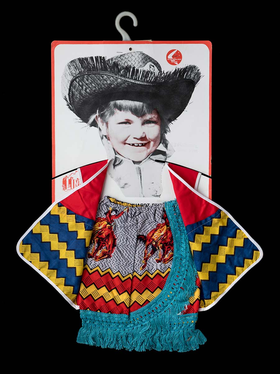 A child's cowgirl costume comprised of a blue and yellow striped vest with red shoulder straps and white edging, and a red and yellow striped skirt with images of people riding horses on a black and white background at the top, and blue fringing. The costume is hanging on a cardboard label with a picture of a child in an Annie Oakley costume, and a plastic hanger. - click to view larger image