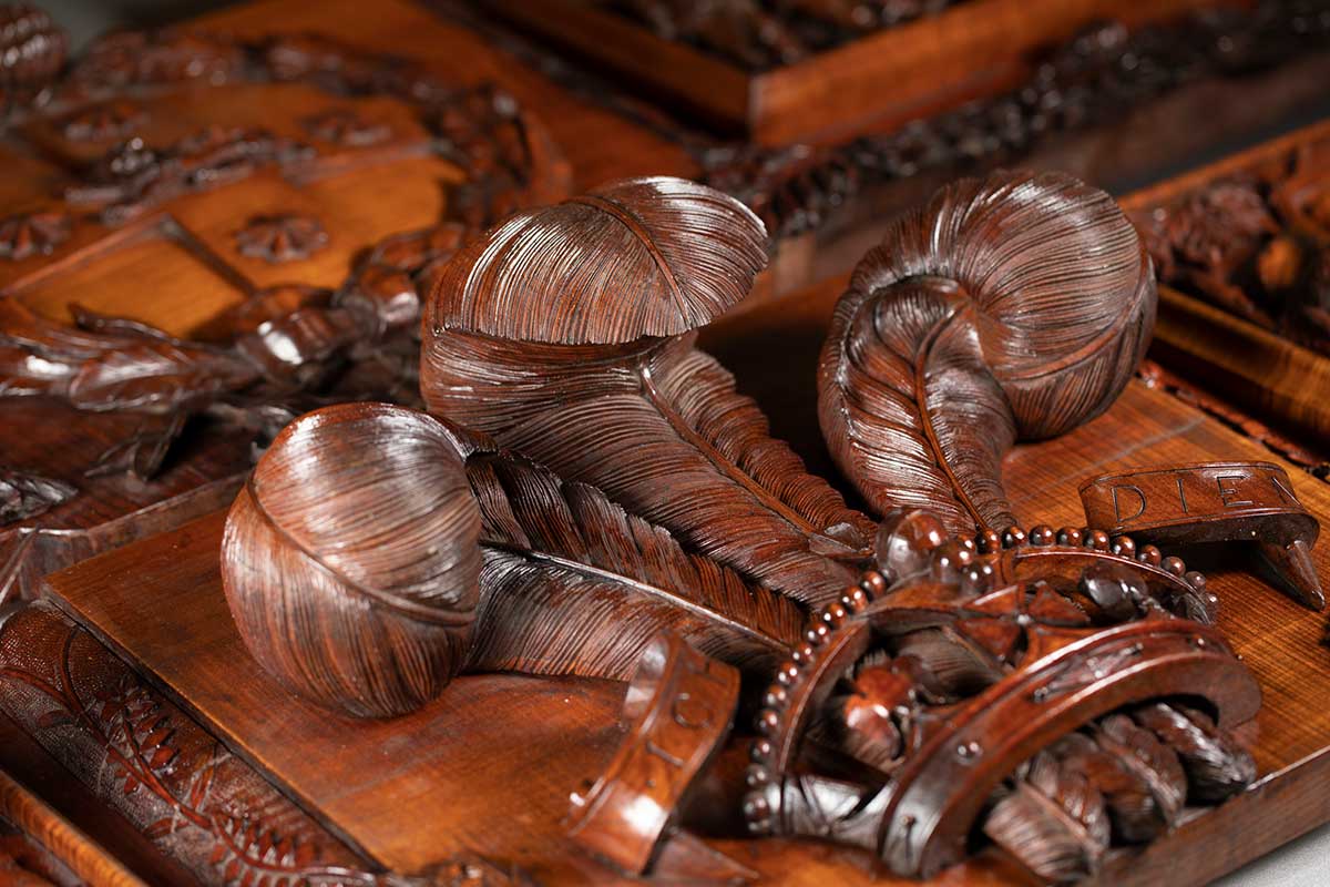Detail of an ornate wooden panel of a relief carving of feathers protruding from a crown. - click to view larger image