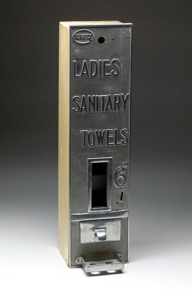 Grey metal sanitary towel dispensing machine with a slot for '6'' coin and coin return near base. - click to view larger image