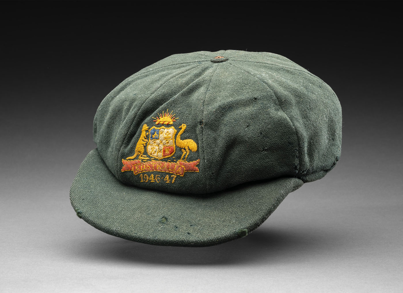 A photograph of a dark green cricket with an embroidered emblem hand stitched on the front. - click to view larger image