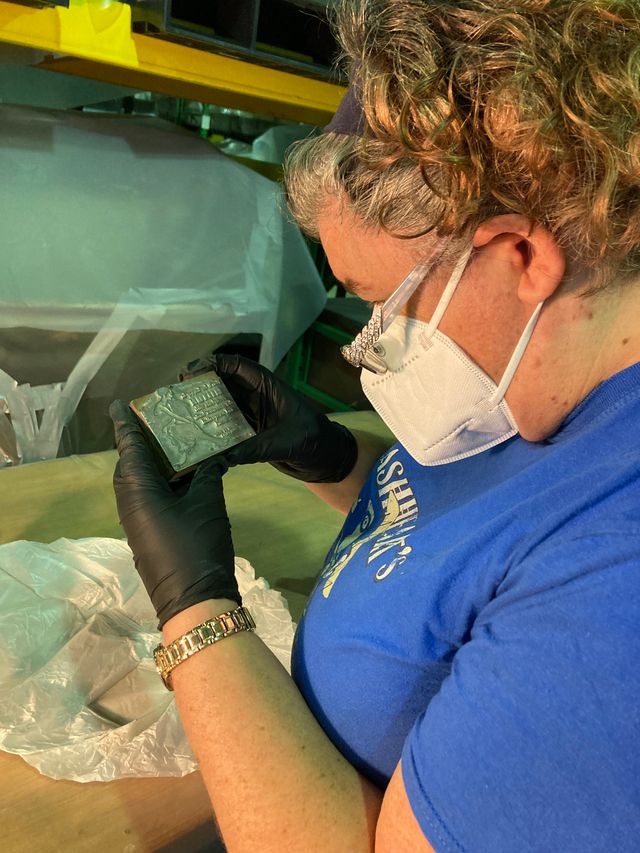A photograph of the person holding a silver object. The person is wearing black gloves and inspecting the silver object.