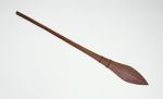 Club made of brown wood with the upper end a paddle-like shape.