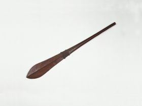 Club made of brown wood that is slightly rhomboid shaped at one end and paddle-shaped at the other. Both ends separated by a pair of bulged rings framing a section of engraving.