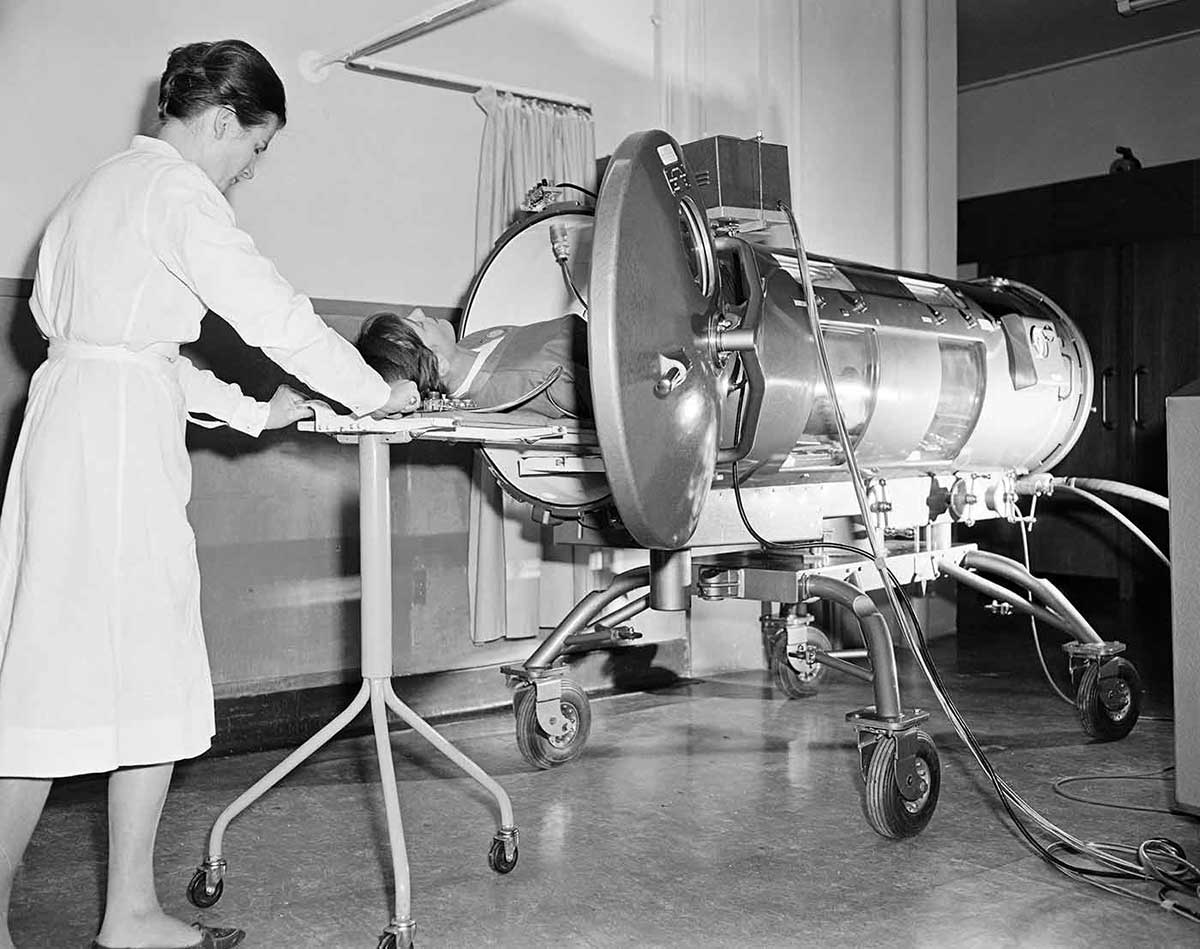 A black and white photo of a female nurse assisting a person inside a lung machine.