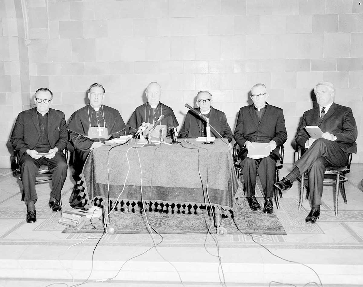 Black and white photograph of a press conference featuring a group of men, some clergymen.