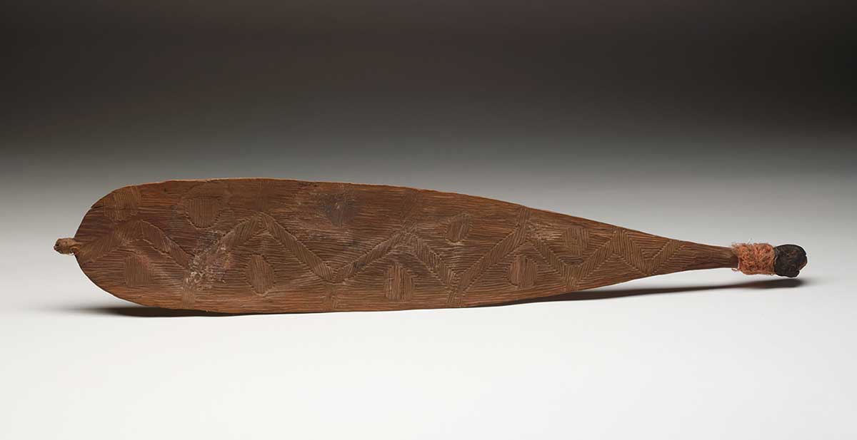 Wooden object resembling a paddle with small handle and zig-zag pattern.