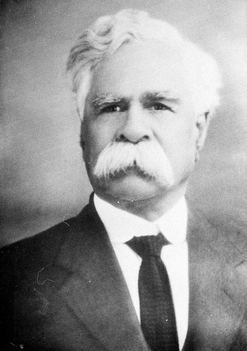 A black and white portrait photo of a white-haired man with a white moustache. - click to view larger image