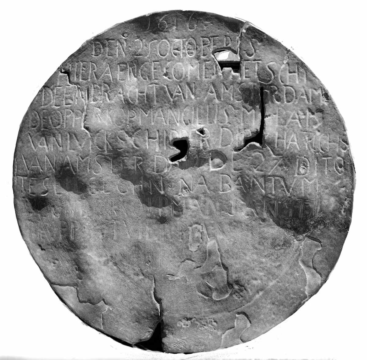 A battered disc, much worn and with holes in it. Words are visible, neatly inscribed in capitals in the top two thirds of the plate.