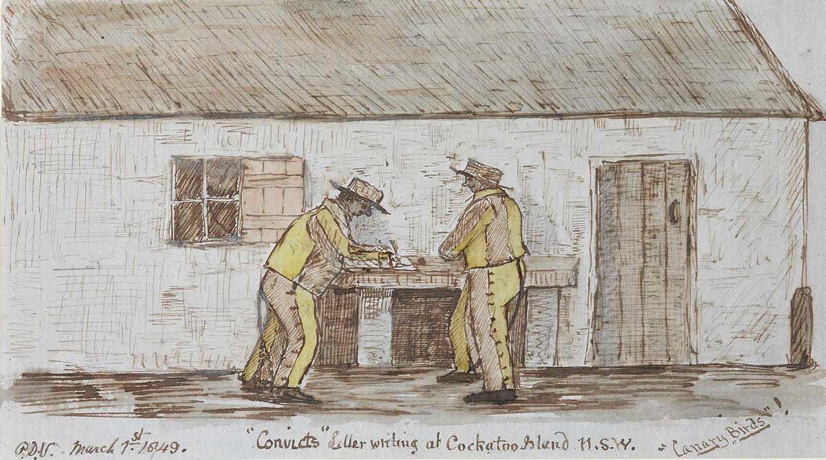 Two men in yellow outfits stand writing at a table immediately outside a cottage.