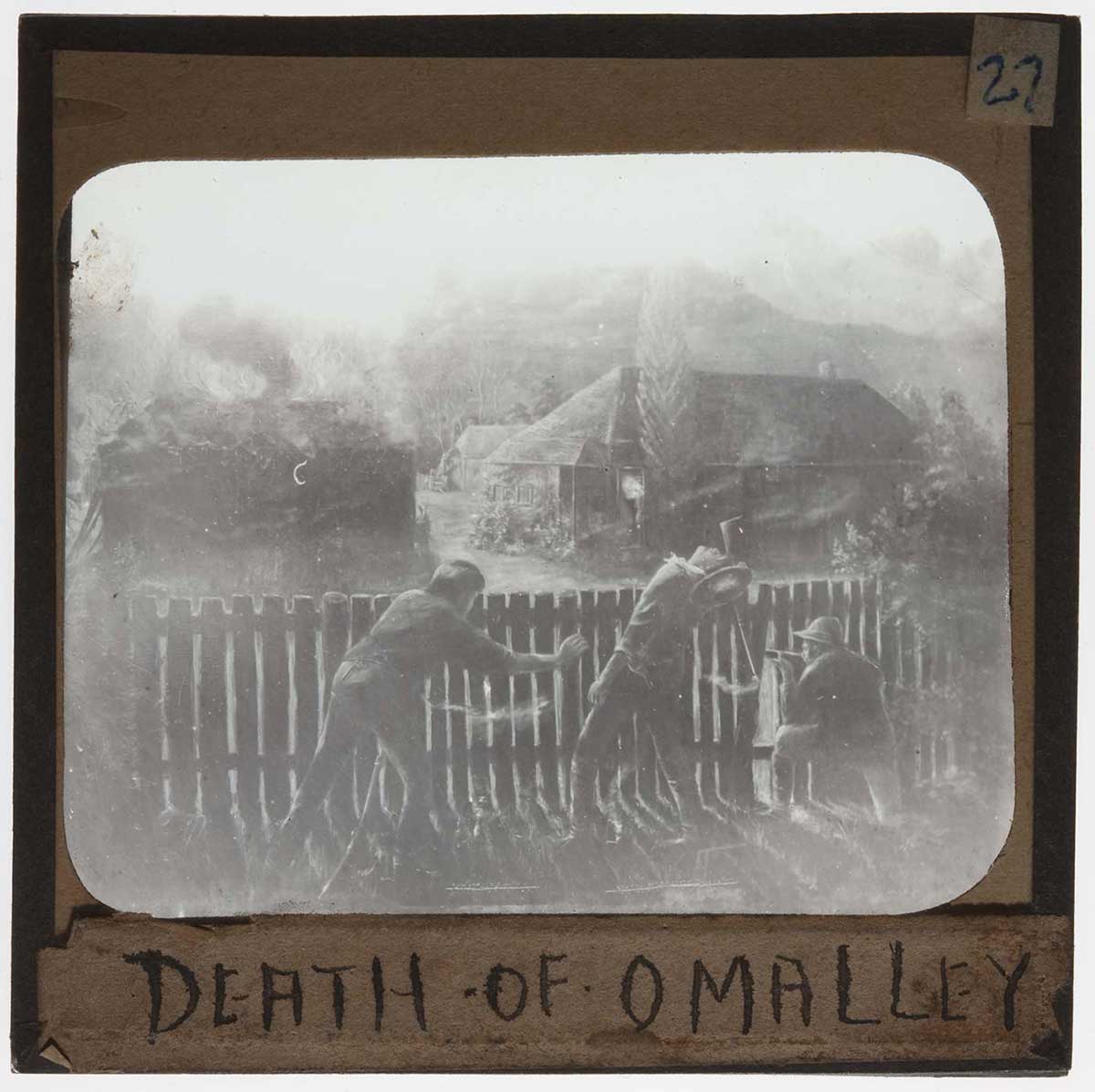 Black and white image of three men crouching behind a fence. The man at centre is reeling backwards. A building burns in the distance. 'DEATH OF O'MALLEY' is handwritten at the bottom of the slide. - click to view larger image