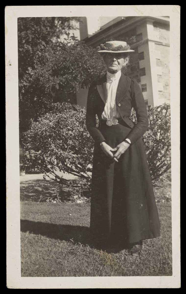 Black and white portrait of Daisy Bates standing in a garden. - click to view larger image