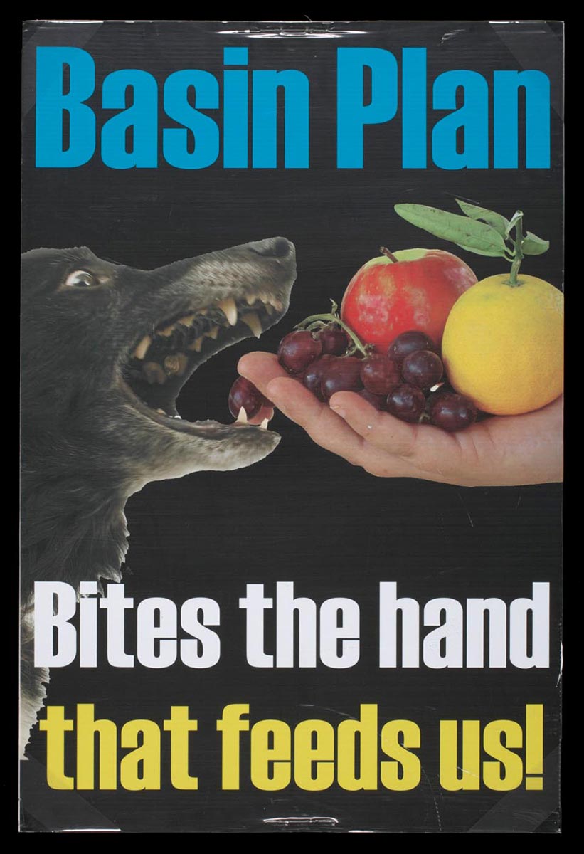 Colour photograph of a poster on a black background, with a central image of a dog biting an extended hand holding fruit. Printed text reads: 'Basin Plan. Bites the hand that feeds us!' - click to view larger image