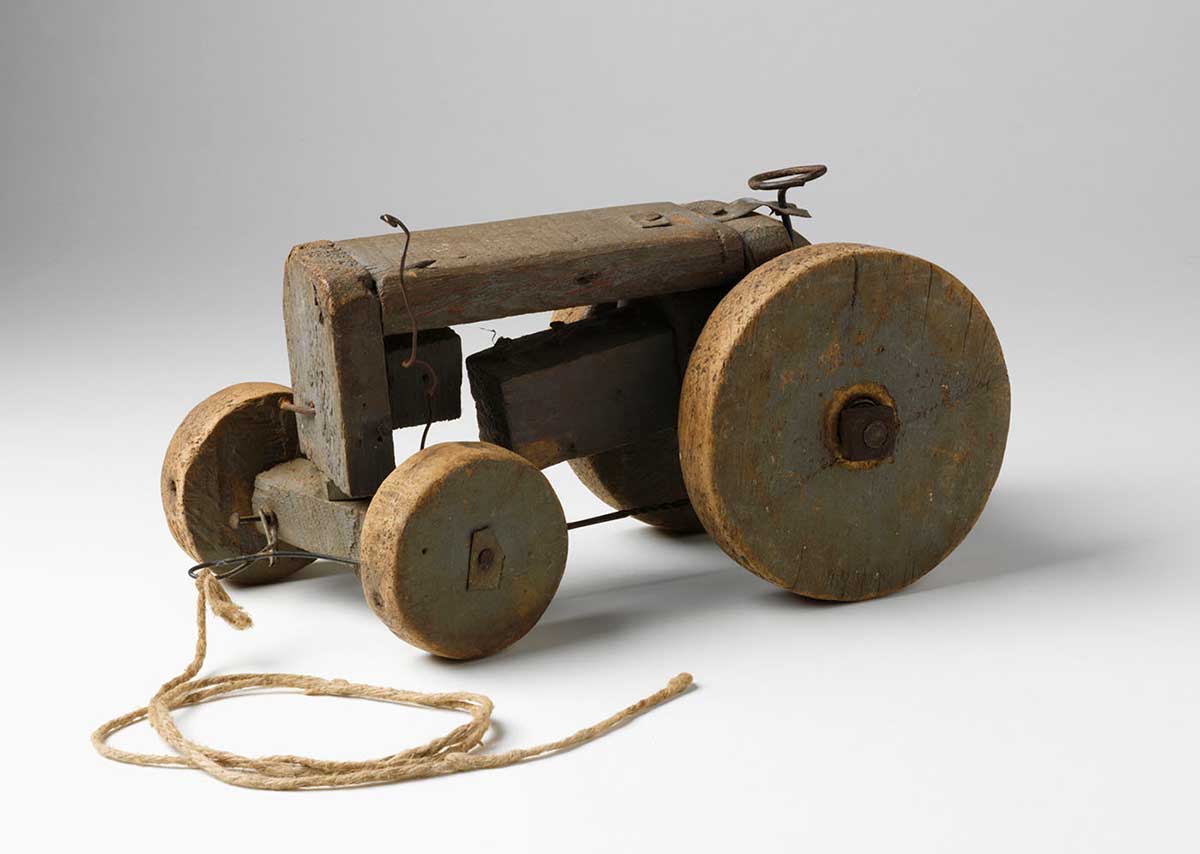 Toy wooden tractor constructed from timber and wire with two larges wheels at the rear and two small wheels at the front.