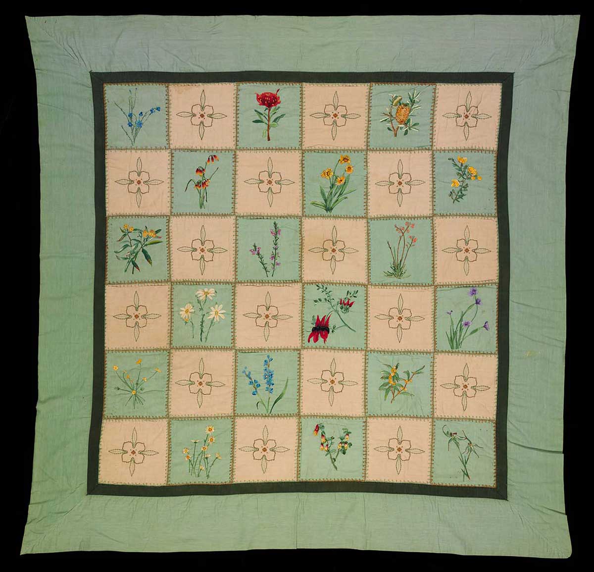 Fabric quilt with green and cream patchwork squares embroidered by hand with Australian wildflower designs, and a recurring passionfruit vine flower design.  - click to view larger image