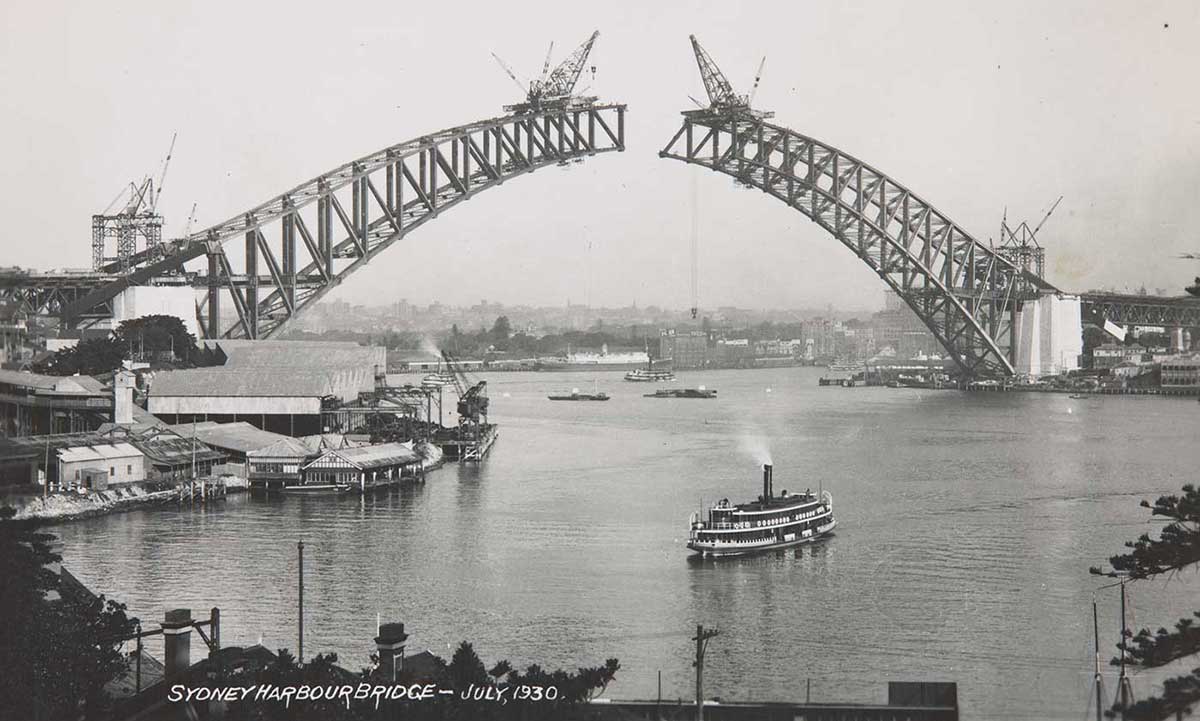 A photo of cranes of on each side of the arch of the Sydney Harbour Bridge before the sides converged in the centre. - click to view larger image