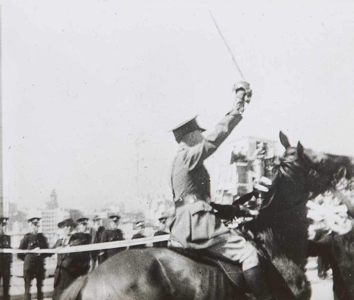 Black and white photo of a man on horseback with sword raised as he approaches a ribbon.  - click to view larger image