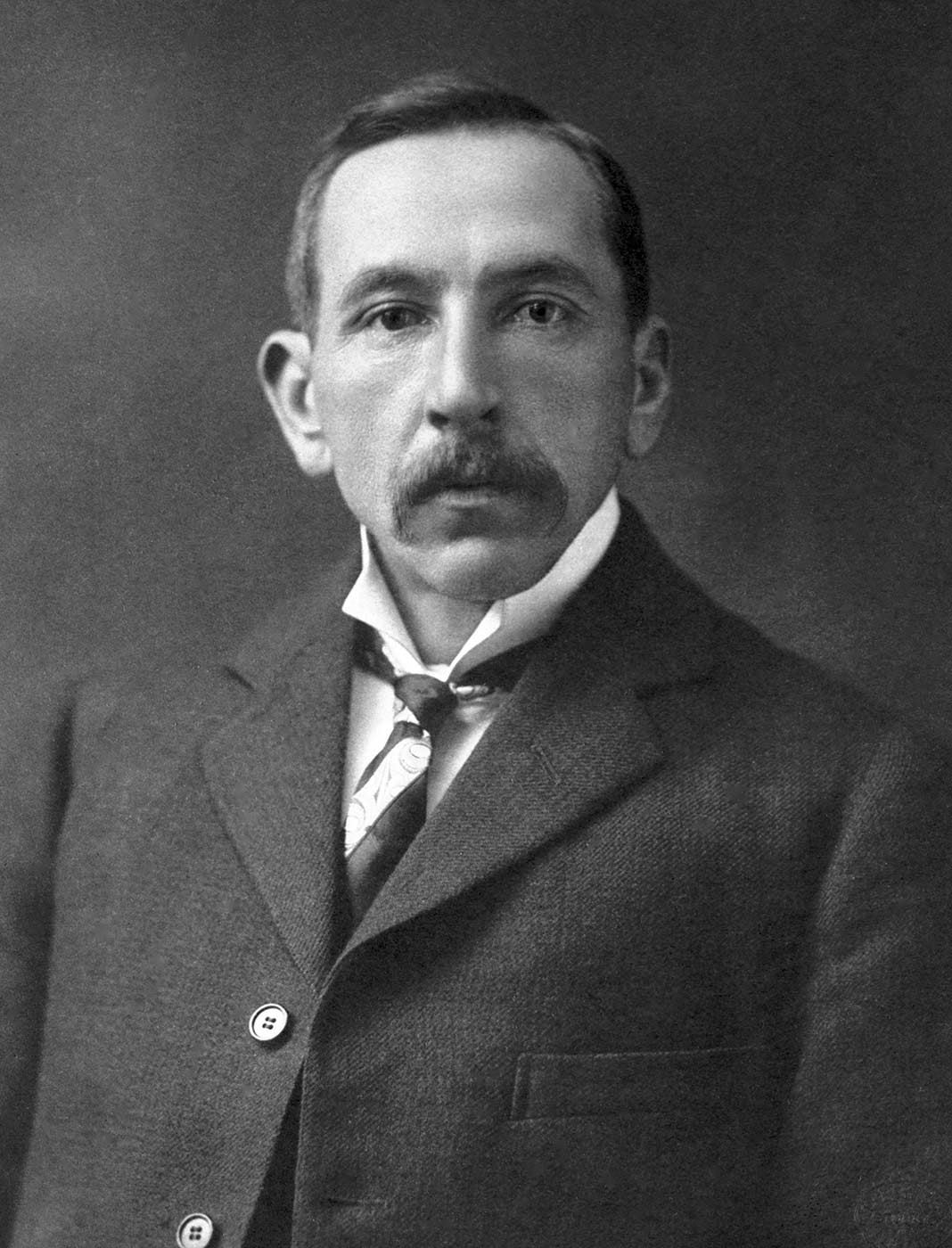 Studio photo of Hughes aged 30 to 40 wearing suit. - click to view larger image