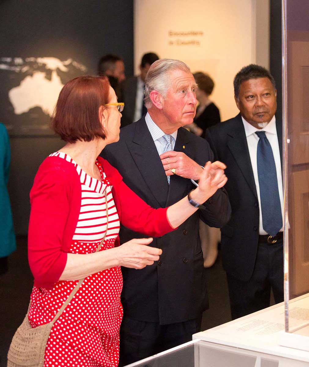 A photo a woman dressed in red with the HRH Prince Charles and another man in a suit - click to view larger image