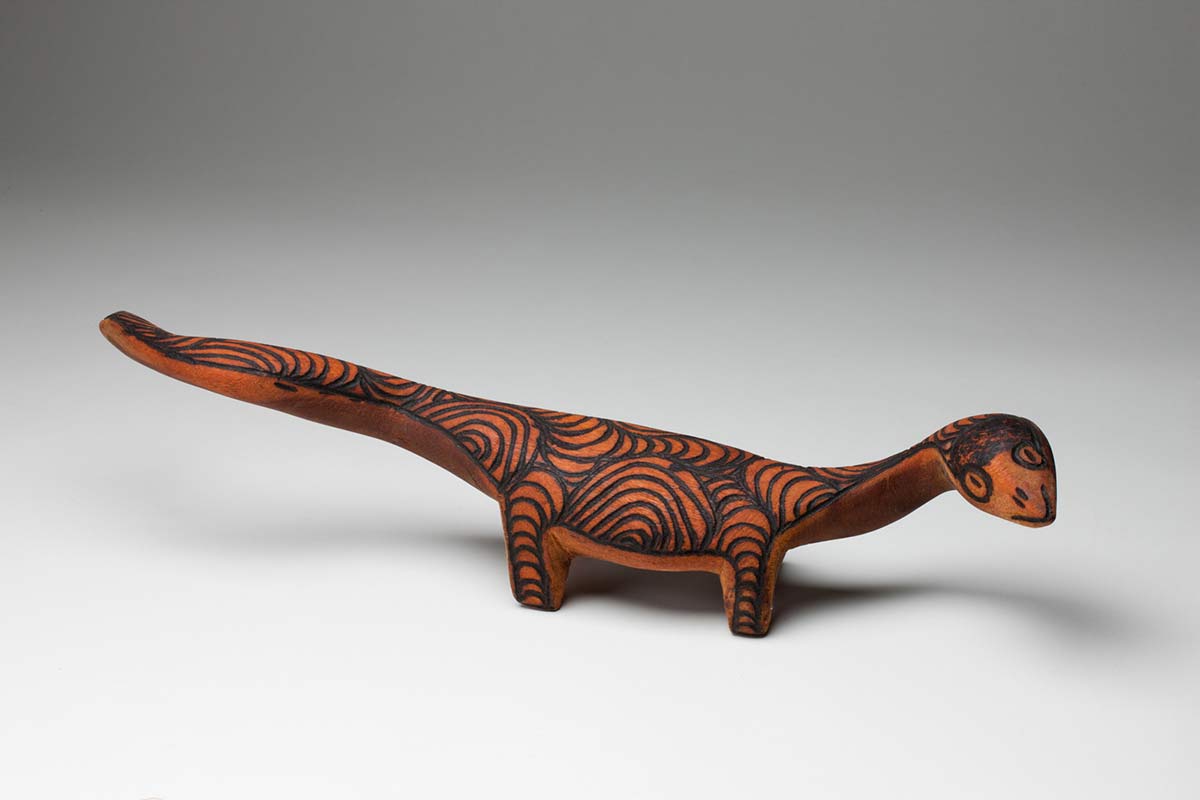 Black and brown wooden goanna sculpture, standing on its four legs. Its head is turned to its right, the tail is turned to its left. - click to view larger image