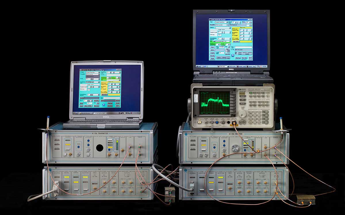An electronic instrument with a silver and blue-green metal and plastic exterior, mounted on a rack. The front panel features various functioning connections and controls. - click to view larger image