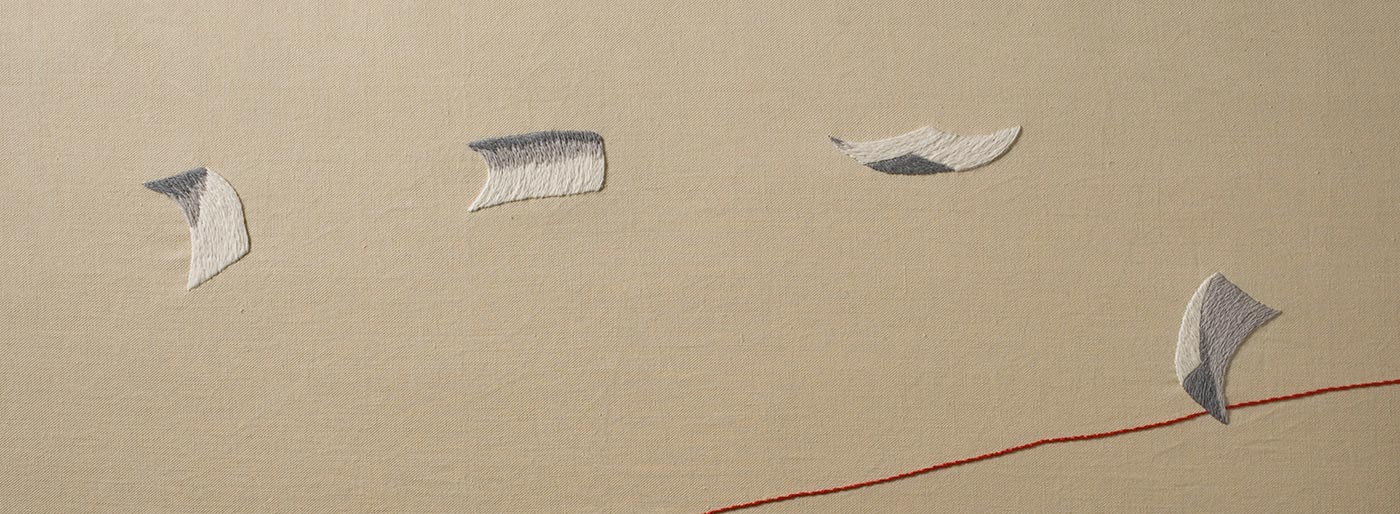 A detail from panel two of 'The Crimson Thread of Kinship' embroidery featuring four pieces of paper trailing across a fawn coloured sky. - click to view larger image