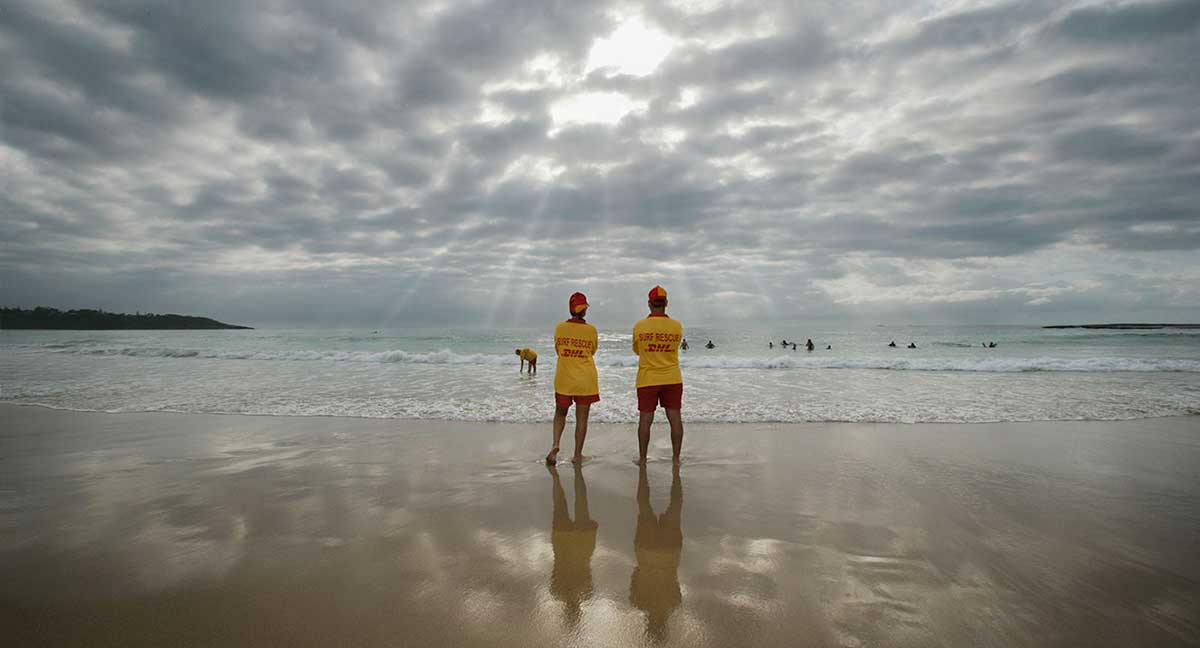 Two surf lifesavers standing on the beach looking towards the surf at Mollymook, New South Wales, 2006. 