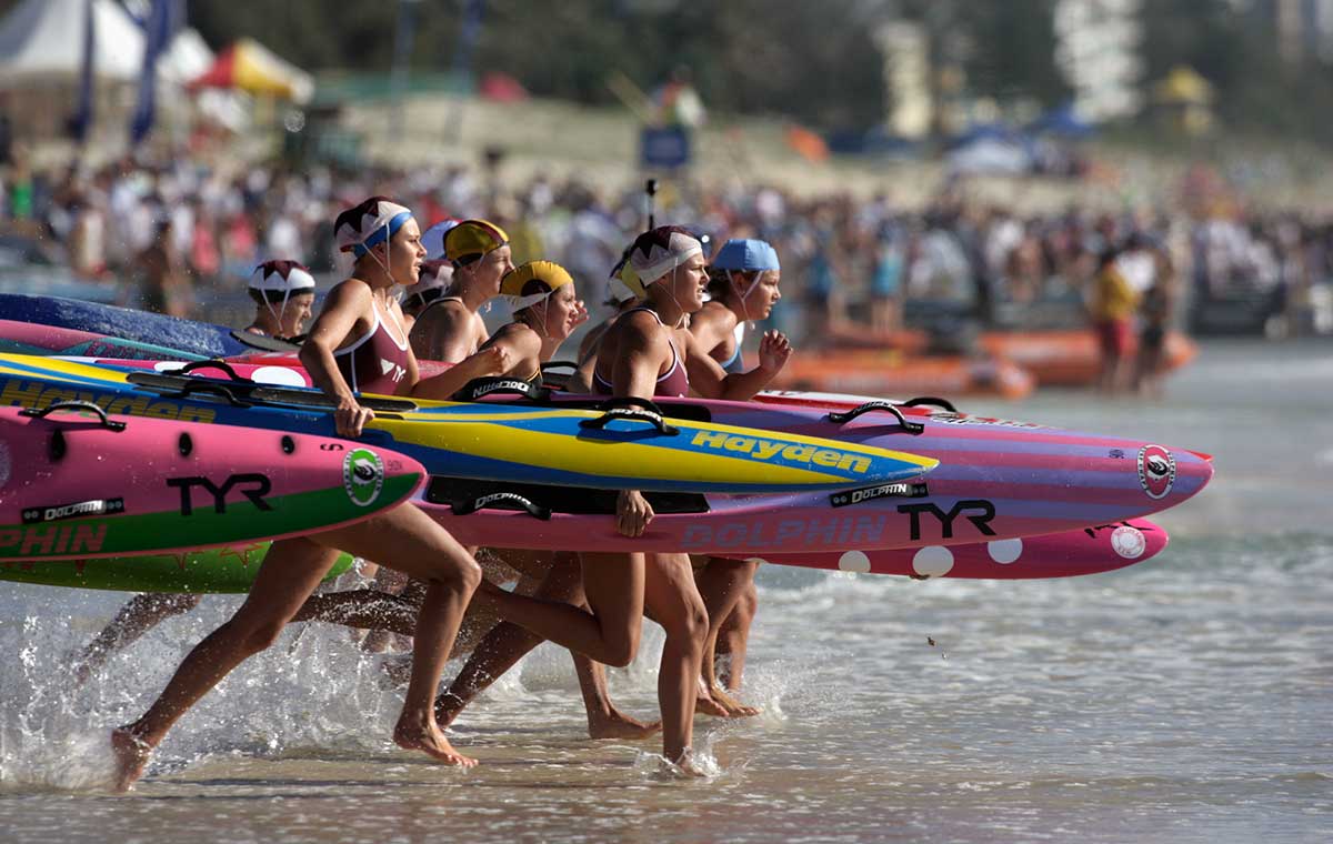 Women carrying surfboards and running towards the surf at the start of a race.