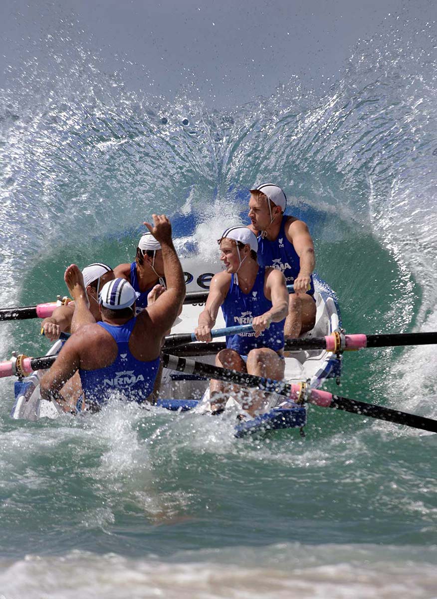 Lifesavers in a surfboat paddling against a large wave. - click to view larger image
