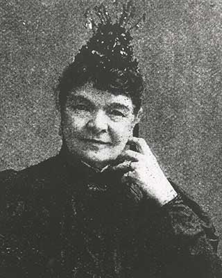 Black and white portrait photo of a woman seated and wearing black attire. - click to view larger image