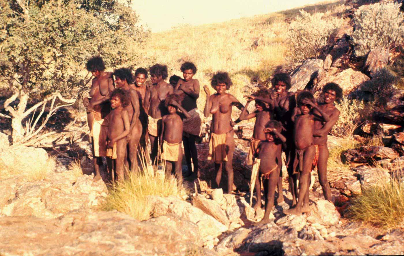 Colour photo of a group of women and children standing amongst bushland.
