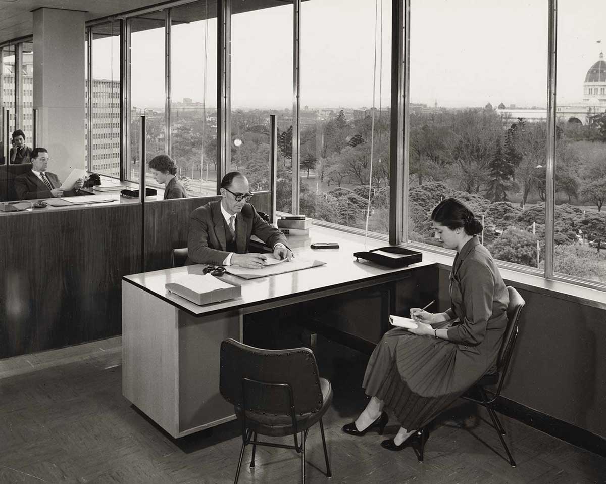 Black and white photo of office workers with a view of parkland from the large windows.