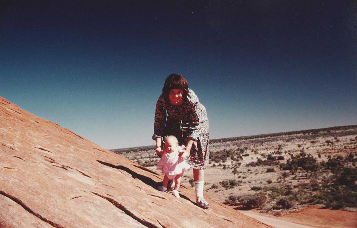 A mother with her daughter poses for the camera while standing on a rock slope in a vast rugged terrain.