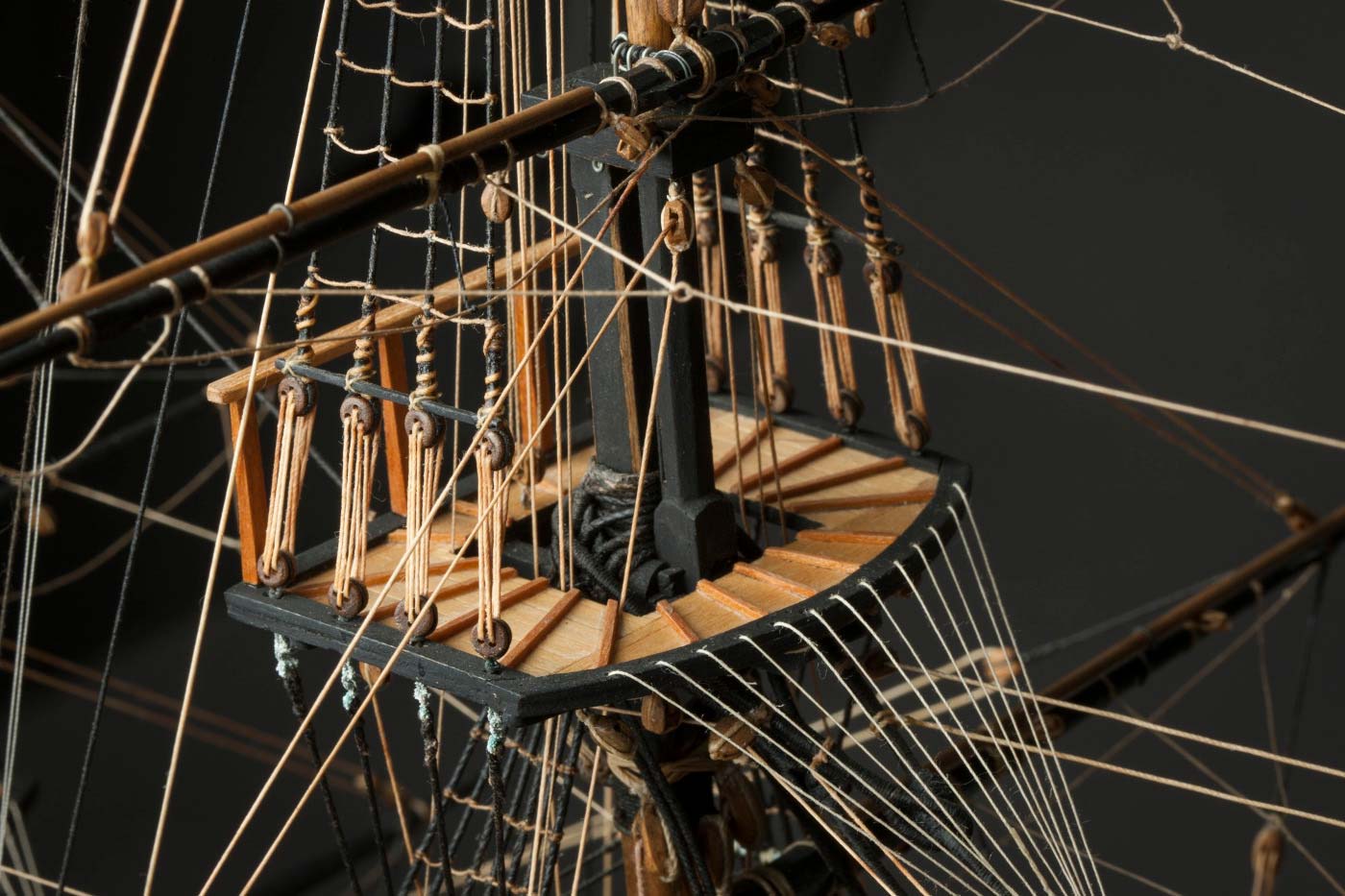 Detail image srom a small wooden sailing ship showing a platform on a mast, surrounded by rope rigging. - click to view larger image