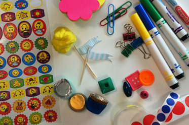 A variety of items that could be used to make a board game including paperclips, stickers, pens, buttons and modelling clay.