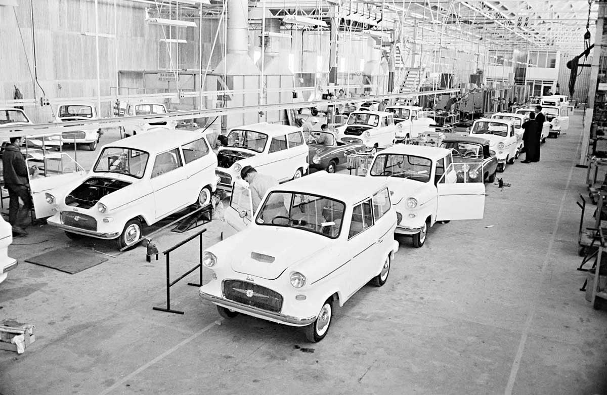 A black and white photo of a row of cars on a mass production line.